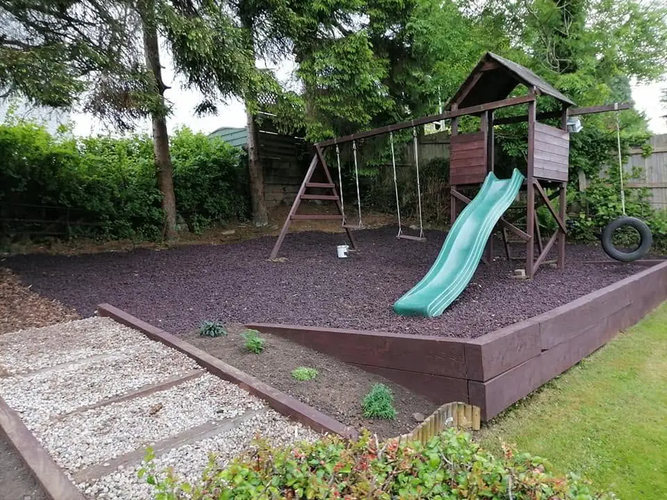 A play area finished with a climbing frame, sleeper edging, dark chippings and a gravel path